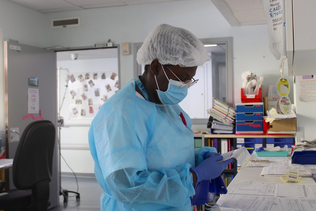 Un agent de santé en blouse, masque et charlotte consulte des documents médicaux dans un service hospitalier à Mayotte